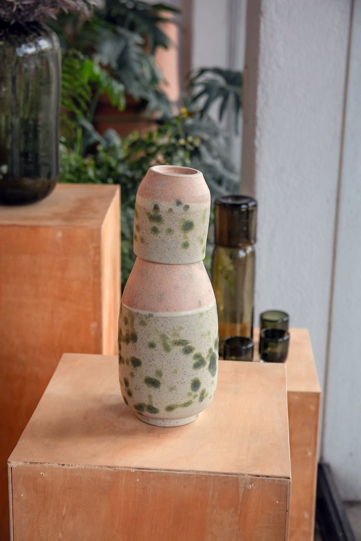 Ceramic vase with speckled design on a wooden surface with plants in the background